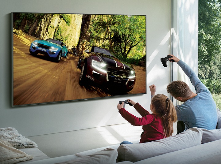 A man and his daughter are playing a Steam game on Samsung Smart TV. The game is being streamed through Samsung Steam Link.
