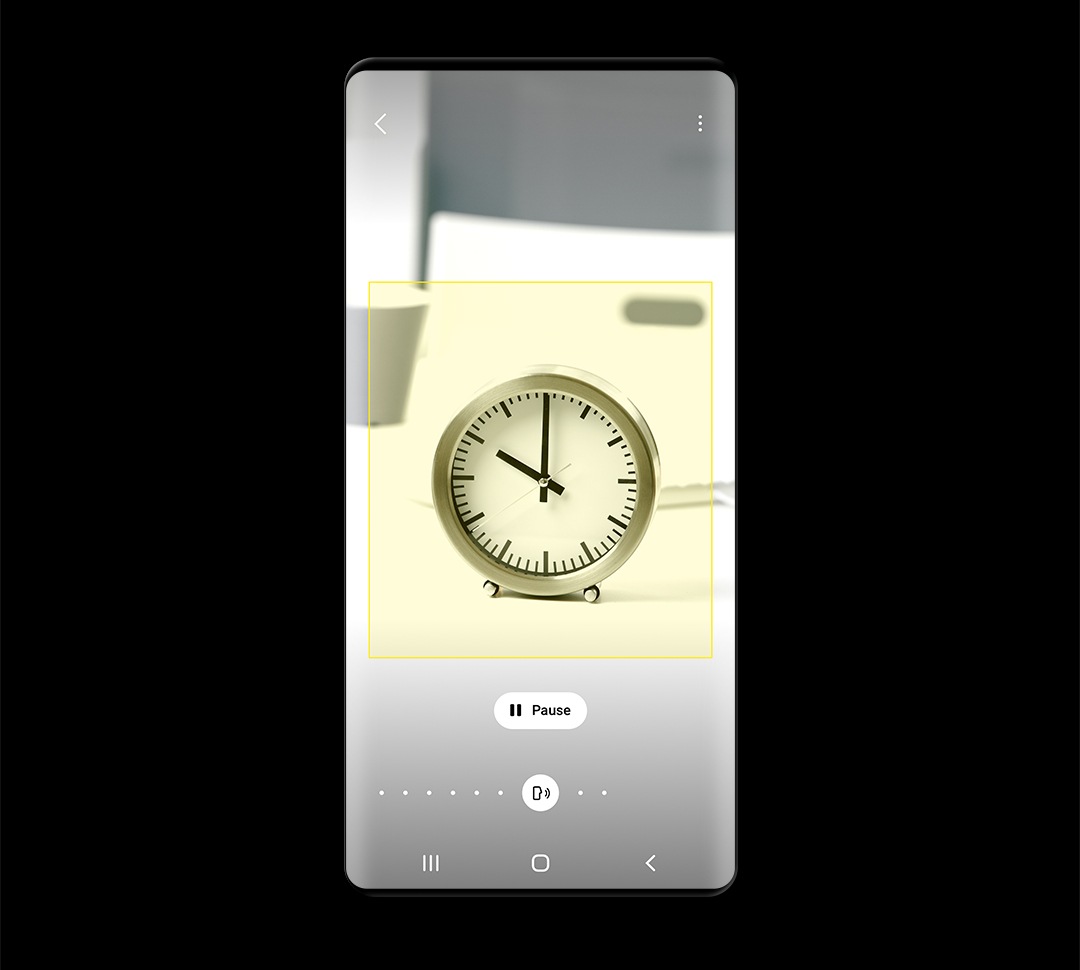 La pantalla de un teléfono muestra un pequeño reloj de escritorio identificado por Bixby Vision, con un botón de pausa debajo de la imagen.