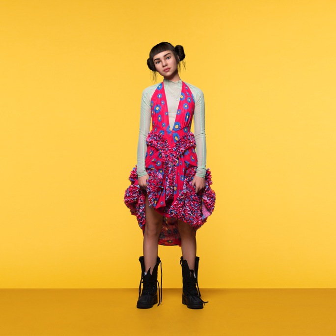 Una fotografía promocional de cuerpo entero de Lil Miquela con un vestido de colores brillantes mientras mira a la cámara con confianza