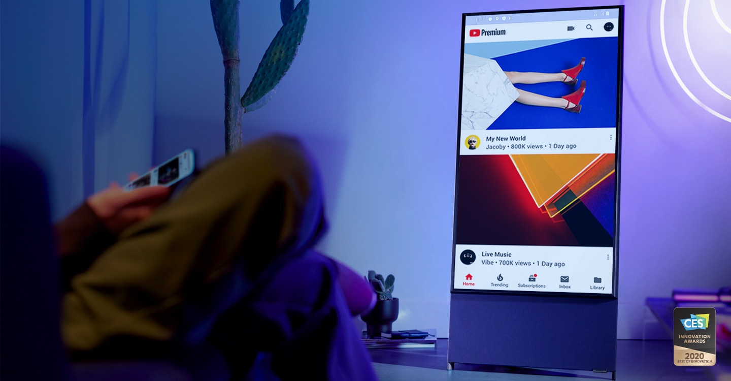 A person is sitting in a chair looking at a cell phone, in front of a YouTube display on the Sero.