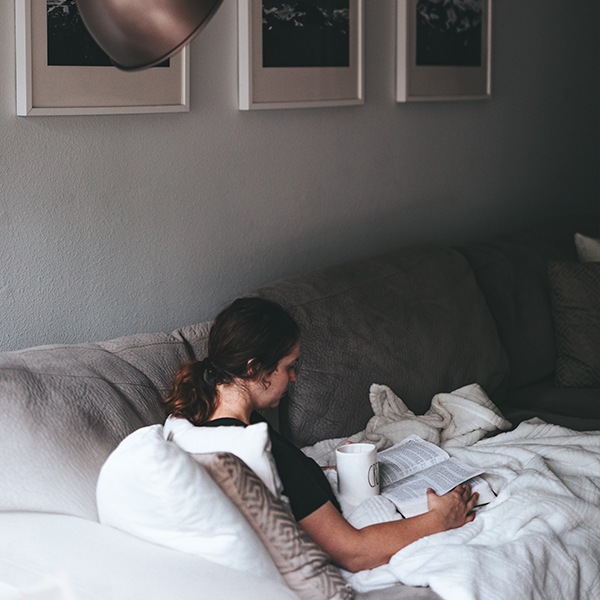 Woman resting on her couch, reading a book with a cup of water