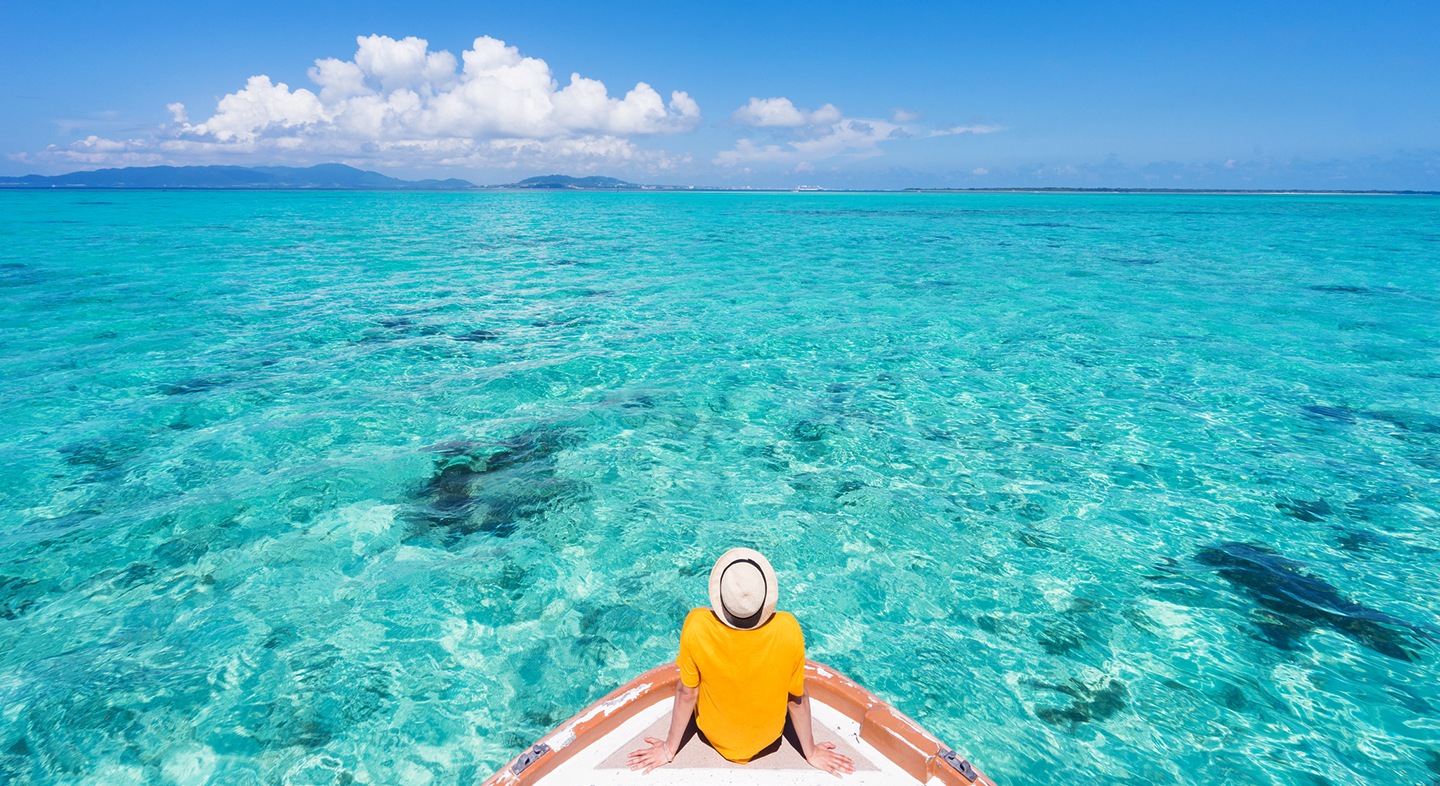 A beach holiday picture of a man sitting on a boat looking at the blue sea.