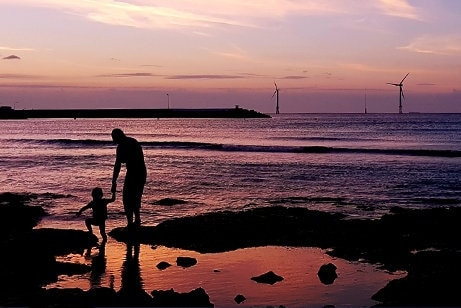 A view of an adult with a child walking on the beach at sunset