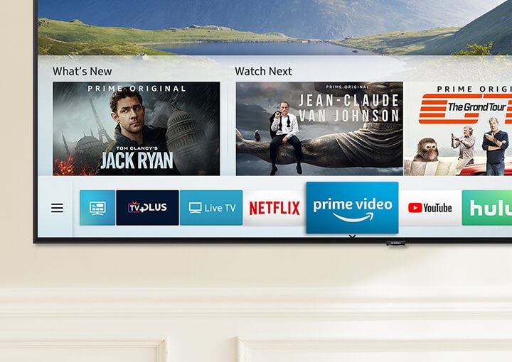 Smart Hub UI is displayed over a nature background image on TV screen; The UI contains various content, such as, 'What's New', 'Watch Next', and several applications like Netflix, Amazon Prime Video, YouTube, Facebook Video, Spotify, Google Play Movies & TV