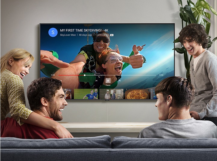 4 people are watching high quality YouTube videos on Samsung Smart TV in the living room. Skydiving video with the 4K logo is being streamed through YouTube app on Smart TV.