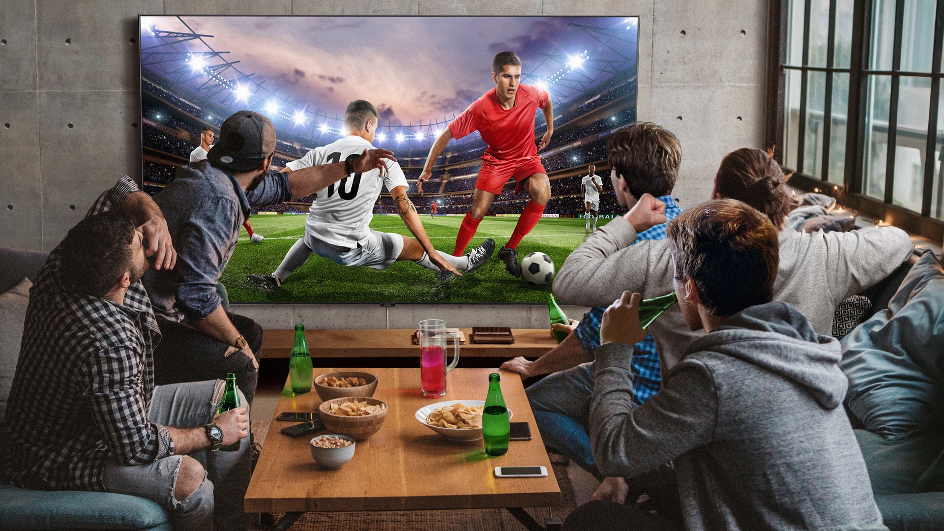 5 men sitting around a mini table with snacks and beverages are watching football game on the large screen TV. With Samsung Super Big TV, size of living space is no longer a factor.