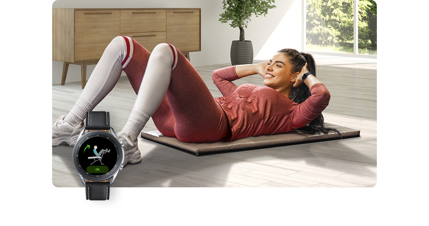 Une femme portant une Galaxy Watch fait travailler ses abdominaux sur un tapis à l’intérieur. Au premier plan, un écran de Galaxy Watch suit ses mouvements.