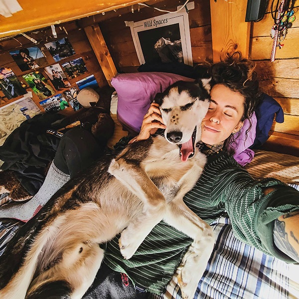 Une fille allongée sur son lit, les yeux fermés, gratte l’oreille de son chien