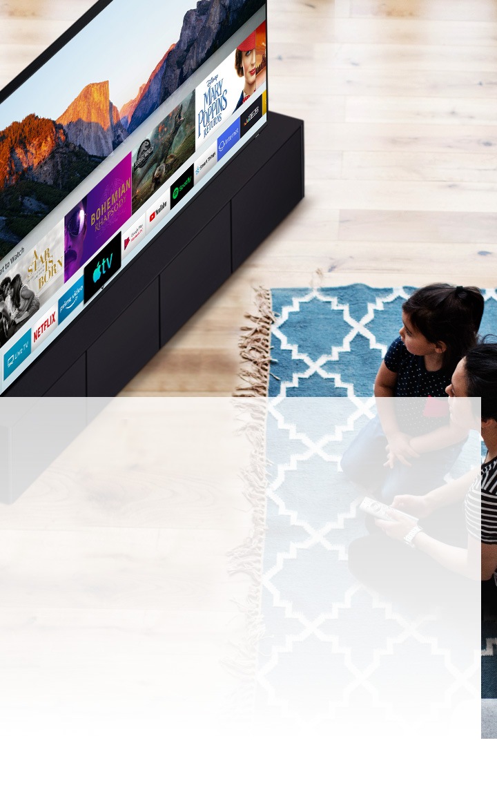Une mère et sa fille sont assises sur un tapis bleu avec des motifs blancs devant un téléviseur intelligent Samsung. Elles regardent les différentes applications installées sur un téléviseur intelligent.