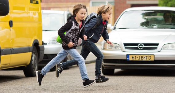 Two young boys running across the street while a car is coming owards them