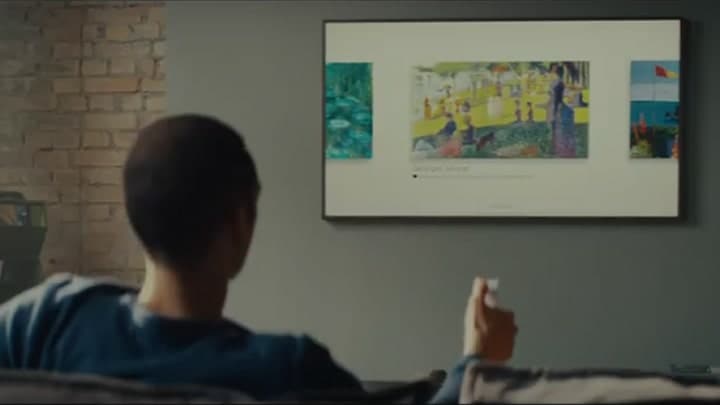 En mann bruker en fjernkontroll for å bla mellom kunstverkene som vises på The Frame som er festet på veggen i stuen.