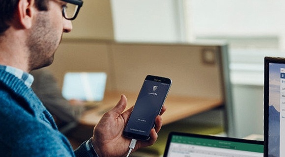 A man utilizing both his Samsung smartphone and desktop device to monitor the transferring process