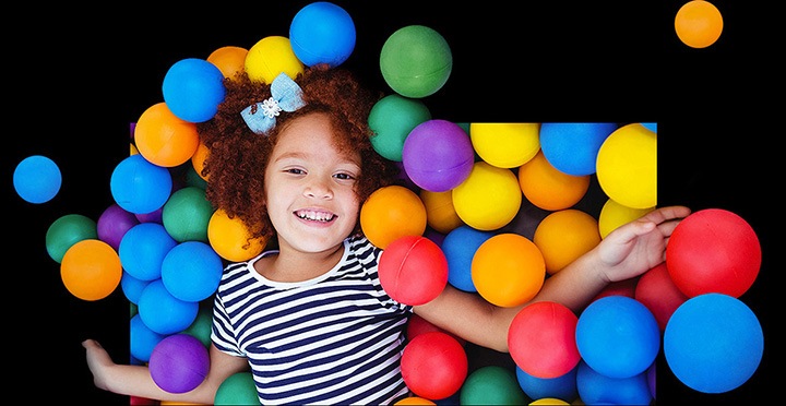 A smiling young girl plays in a ball pit filled with multi-colored plastic balls.