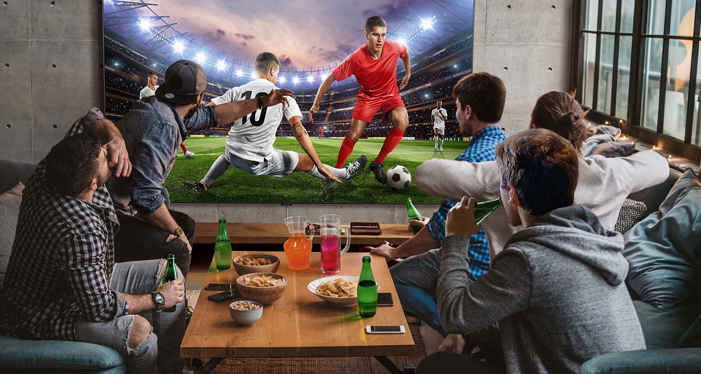 5 men sitting around a mini table with snacks and beverages are watching football game on the large screen TV. With Samsung Super Big TV, size of living space is no longer a factor.