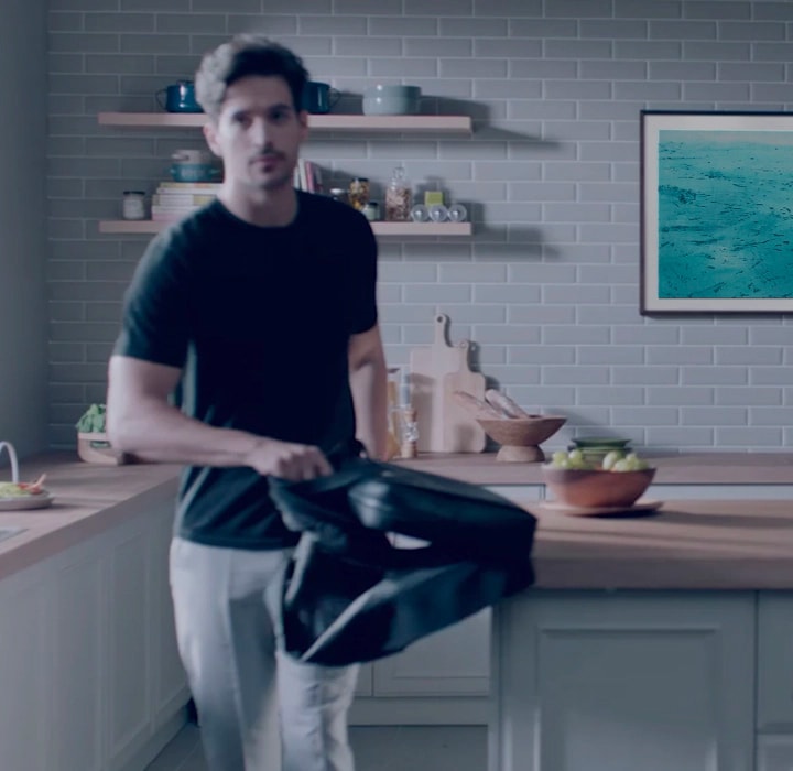 A man is in the kitchen and The Frame TV is on the wall behind him displaying a painting. The Frame TV automatically turns off after he leaves the room.