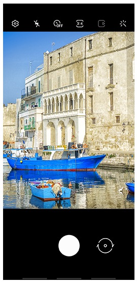 Se muestra la pantalla de la cámara del teléfono inteligente con un enfoque en botes azules flotando en el agua frente a edificios de estilo europeo.