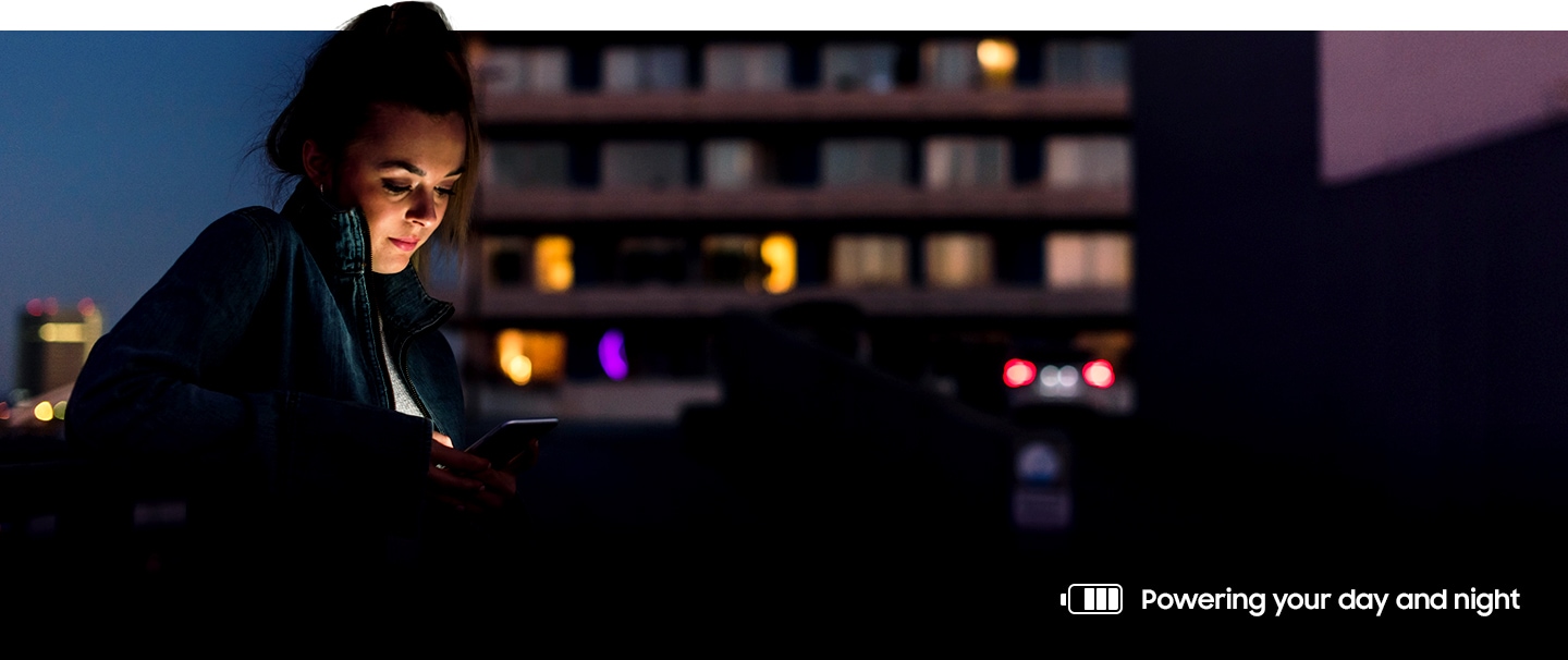 Image of a woman using her phone outside at night. A battery icon on the bottom right shows she has most of her battery power left.
