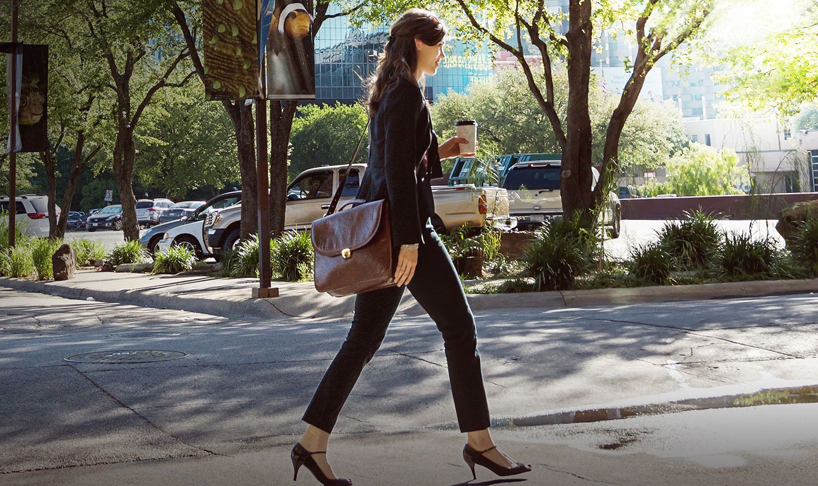 Background image of woman walking in the street holding coffee wearing Gear IconX
