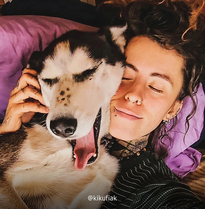 Girl laying on the bed, eyes closed, with her dog and scratching the dog's ear