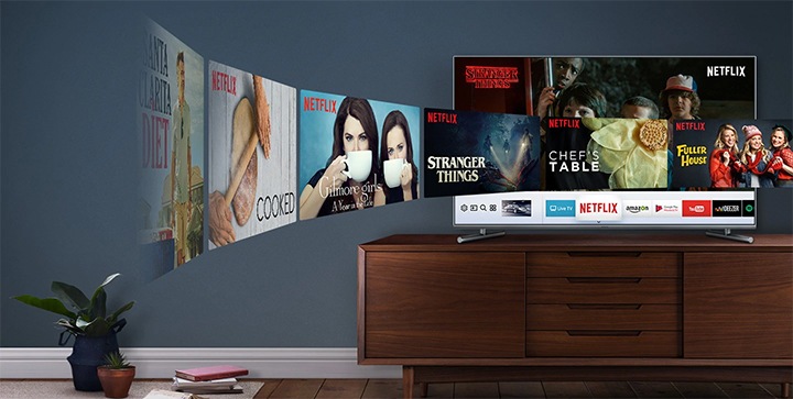 Smart TV stoi na szafce, na ekranie widać różne aplikacje i tytuły filmów.