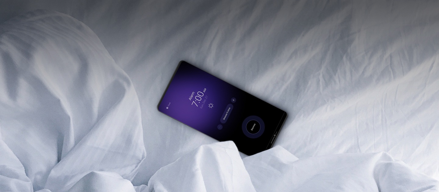 Um smartphone Galaxy com lençóis brancos com o alarme das 7 horas a tocar.