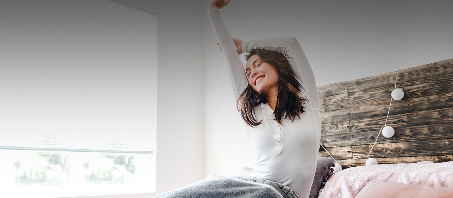 Uma mulher acordando, espreguiçando-se na cama com um sorriso.