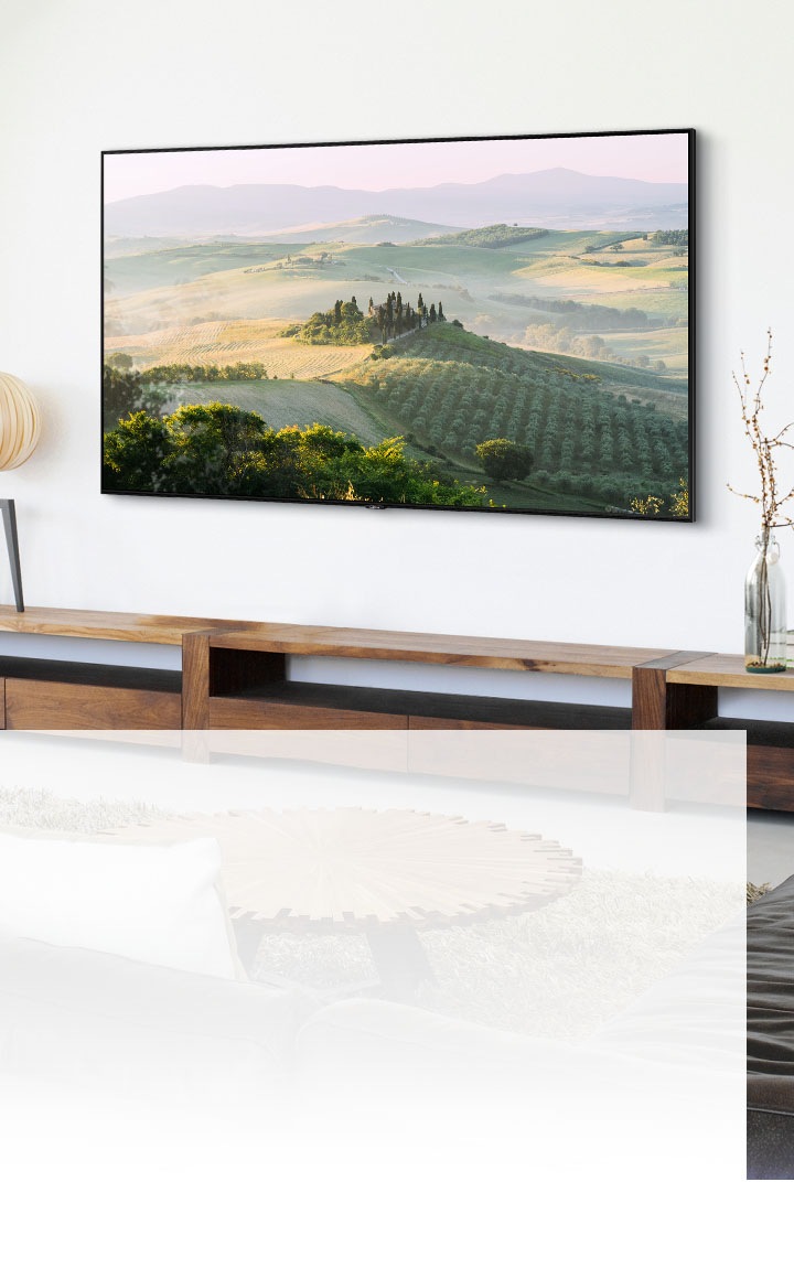 Un televisor de pantalla grande colgado en la pared muestra un paisaje de campo en una sala de estar iluminada con luz natural.