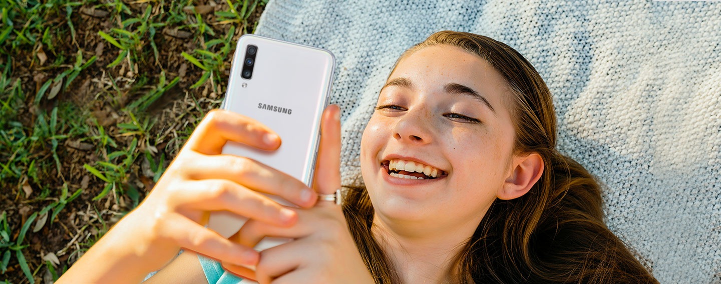Slika žene kako leži na ćebetu na otvorenom i koristi Galaxy A.