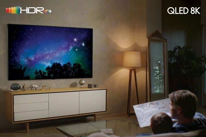Отец с сыном отдыхают дома перед телевизором. Логотип HDR10+ в верхнем левом углу и логотип QLED 8K в верхнем правом углу.