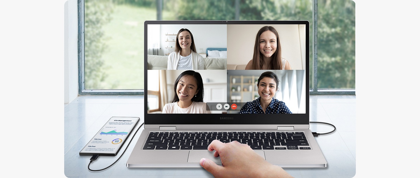 A smartphone is connected to a laptop. The laptop screen shows a conference call with four other people while the smartphone shows a completely different screen.