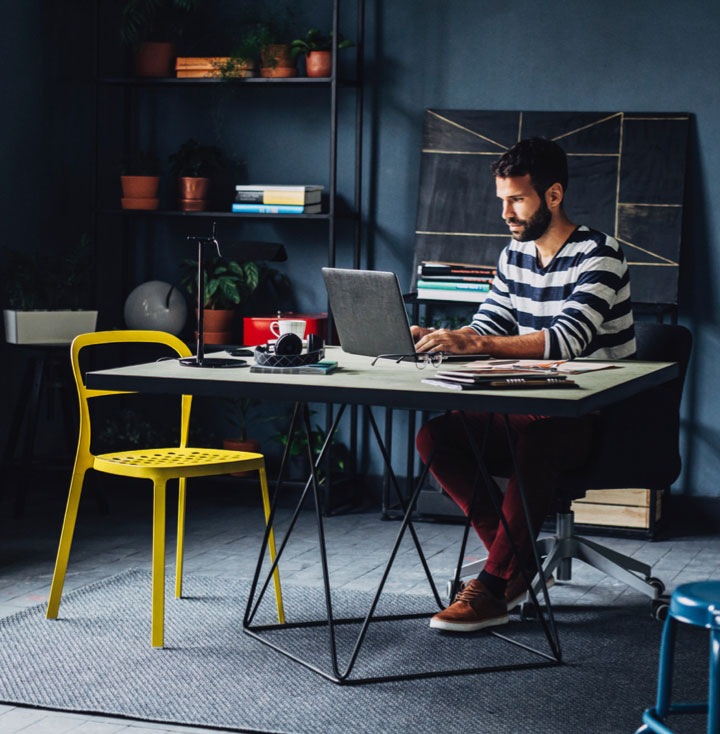 A wide shot of a man sitting at a desk, he is in a large room that seems to be his home office