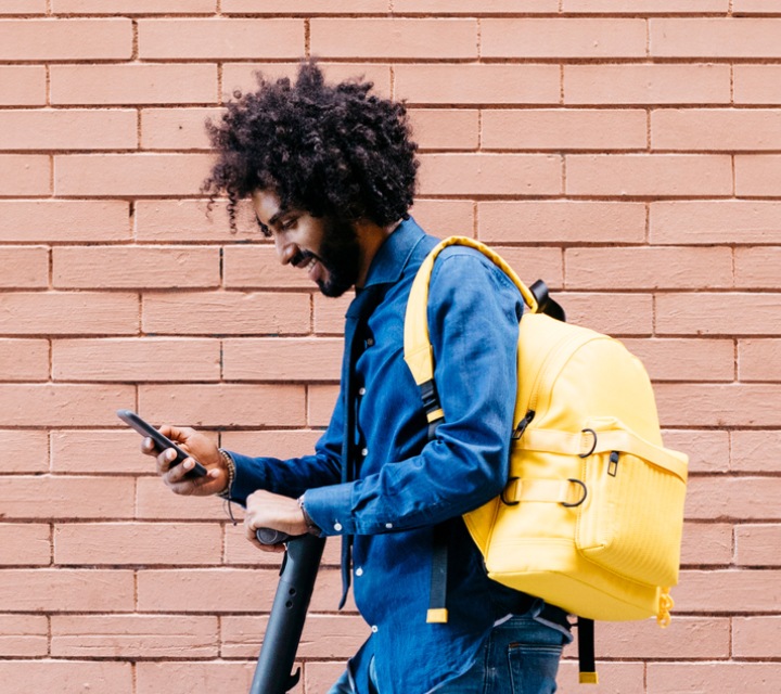 We see a man on a scooter wearing a backpack stops to check his phone.