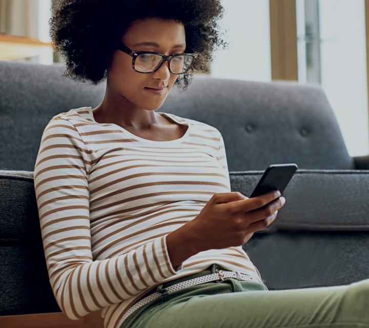 A young woman sitting on a couch looks down at her phone.