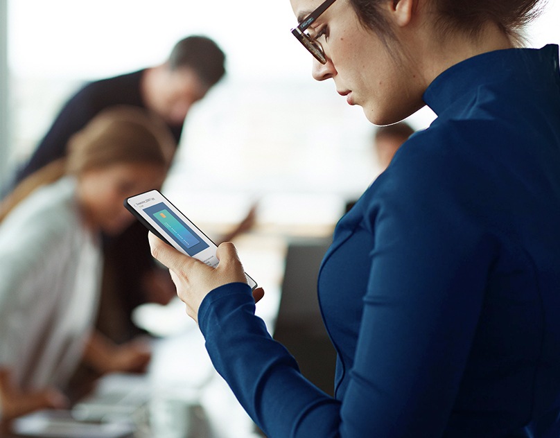 I den mörka bakgrunden finns en kvinna med sin smartphone. I förgrunden visar två Galaxy smartphone-skärmar hur privat delning låter användaren ställa in och ändra den giltiga varaktigheten för hur länge delade filer kan visas.