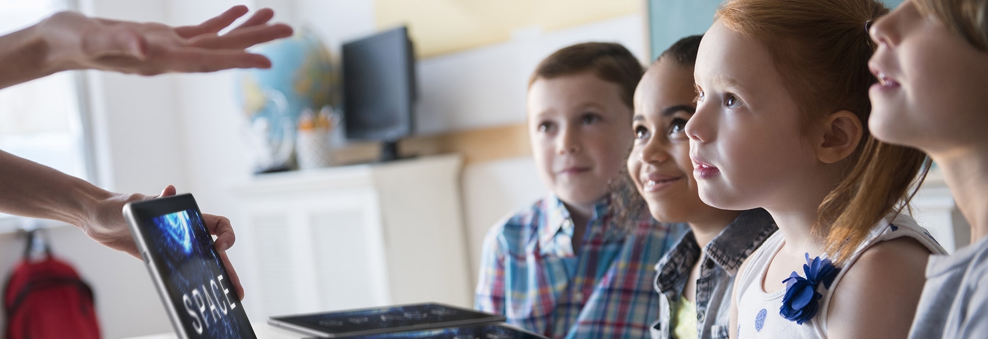 An image of a user’s hands over a Galaxy Book 10.6 device’s screen, with children sitting facing the device, listening to what the user is saying.