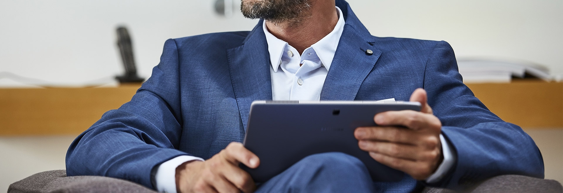 An image showing a seated man in a blue suit, holding a Galaxy Book 12 device.