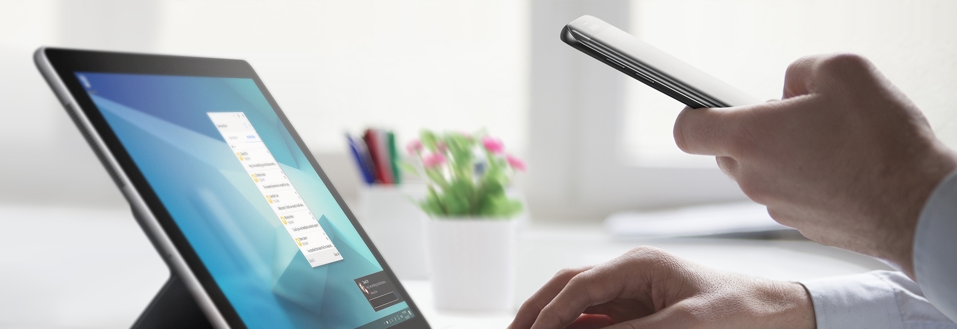 An image showing a user using a Galaxy Book 12 device with one hand, and using a smartphone with the other hand.