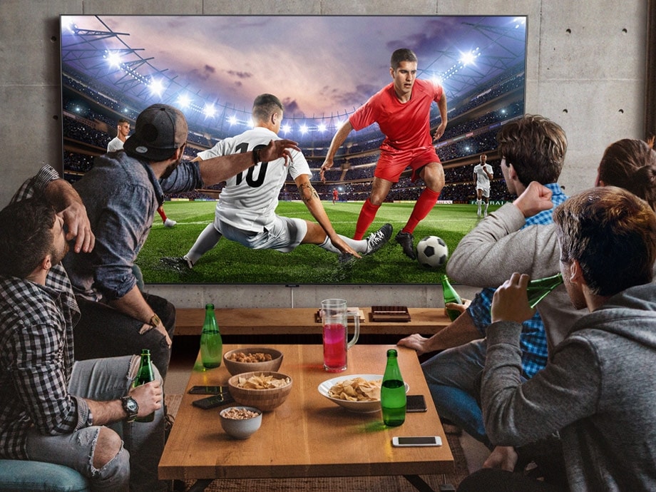 다섯 명의 남자가 간식과 음료가 놓여진 미니 테이블 주위에 둘러 앉아 초대형 TV로 축구를 보고 있다. 삼성 Super Big TV라면 시청 공간의 제약이 줄어듭니다.