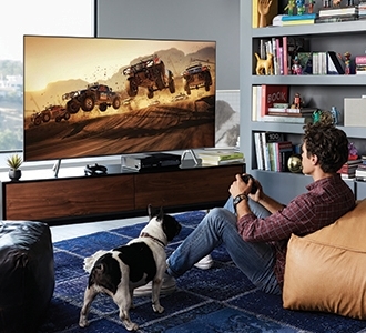 2018 QLED TV Q6F의 라이프 스타일 이미지입니다. QLED TV가 거실 테이블 위에 놓여있고, 한 남자가 QLED TV로 게임을 하고 있습니다.