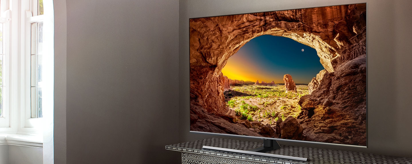 QLED 4K QT70 시리즈 제품 이미지입니다. 회색톤의 방에 놓여있는 콘솔 위에 TV 제품이 놓여있으며, 이미지 왼쪽에 있는 창문에서는 햇살이 비춰 들어옵니다. 이미지 좌측에 빛을 넘어서는 QLED 4K 문구가 적혀있습니다.