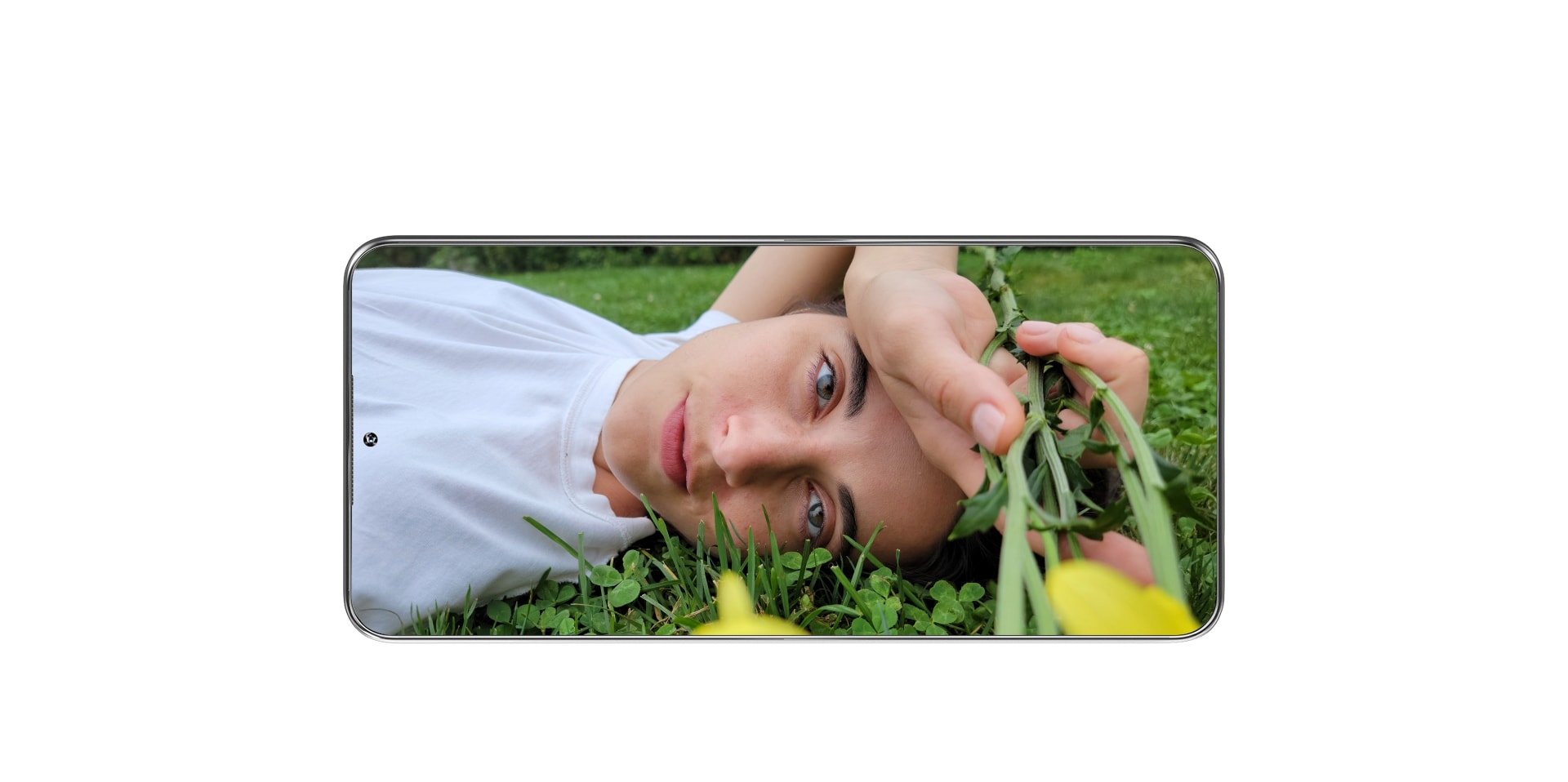 An image of a person lying on the grass and holding a flower on the screen of a smartphone.