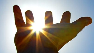 Hand reaching up toward the sky, with the sun seen between its fingers.