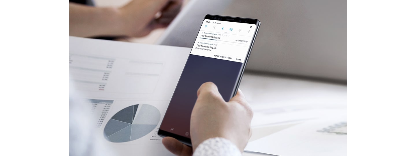 Image of a person holding Galaxy Note9 with the download GUI onscreen, one download is finishing and another is completed