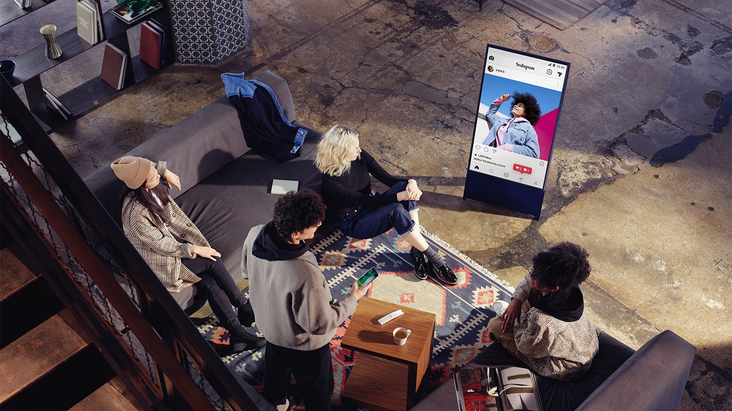 gallery image 6 Four people are sitting in a large stylish living room with The Sero placed in portrait mode directly in front of them, mirroring one of their Instagram feeds.