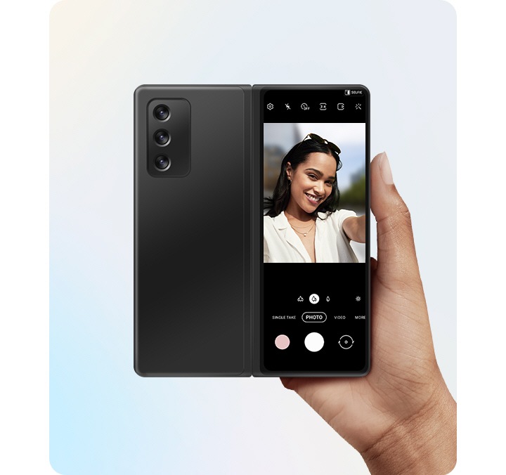 Uporabnik dvigne razprt Galaxy Z Fold2 mobilni telefon ter ga z glavno kamero in zunanjim zaslonom obrne proti vam. Predogled na zunanjem zaslonu prikazuje možnost preprostega ogleda selfija v realnem času s funkcijo Selfi z glavno kamero.