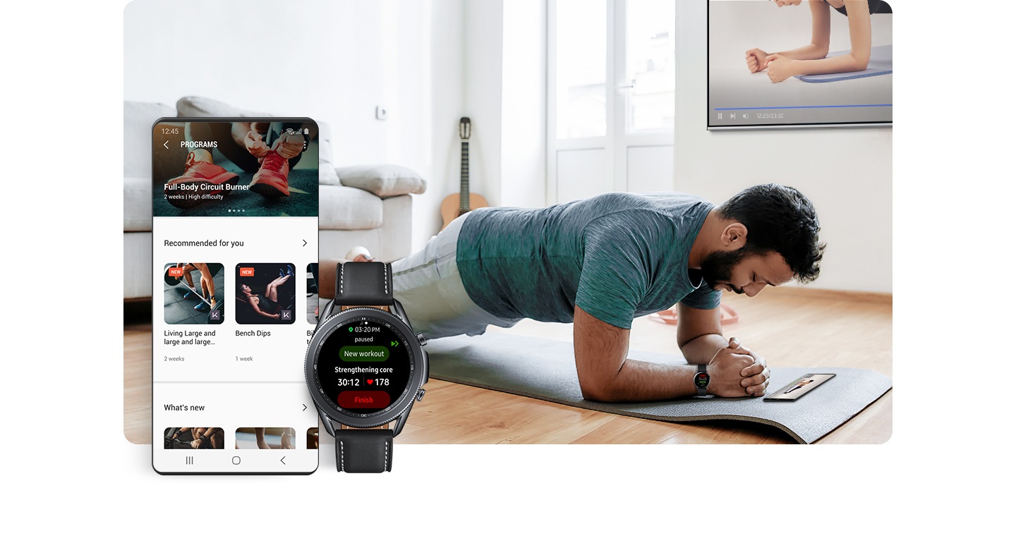 ผู้ชายคนหนึ่งที่สวม Galaxy Watch อยู่นั้นกำลังทำท่าแพลงก์อยู่บนเสื่อออกกำลังกายในบ้าน โปรแกรมการออกกำลังกายของเขาแสดงอยู่ในสมาร์ทโฟนบนพื้นและในทีวีบนผนัง ที่ด้านหน้าของภาพมีหน้าจอ GUI ที่แสดงให้เห็นถึงโปรแกรมการออกกำลังกายต่าง ๆ ปรากฏขึ้นมา หน้าจอ Galaxy Watch แสดงผลชื่อของการออกกำลังกายและอัตราการเต้นของหัวใจ