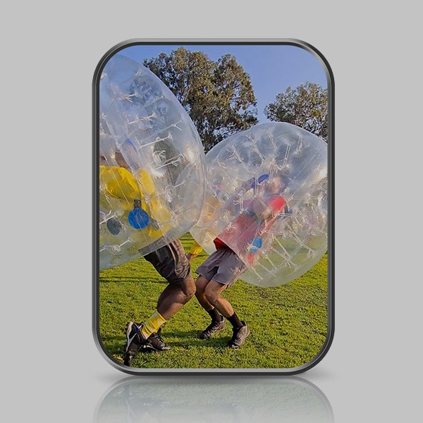 Two men are colliding on an outdoor soccer field in inflatable bubble bumper suits. Their knees are slightly bent.