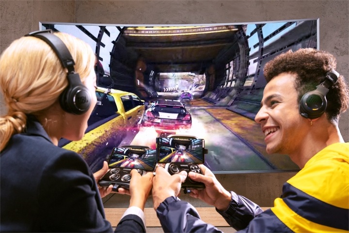 A man and a woman with headphones on and smartphones connected to a tv, using them as controllers for a game on the large screen
