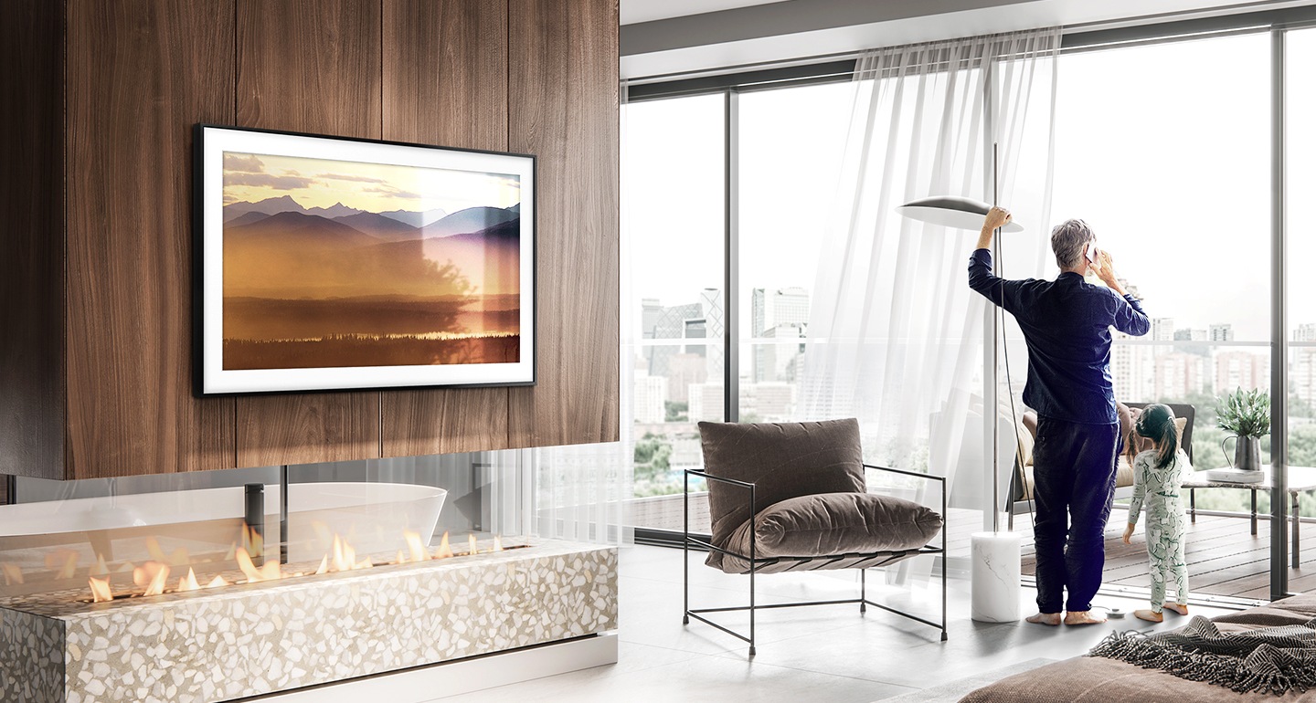 Bir adam ve çocuk terasa bakan oturma odasında ayakta durmakta. Samsung Frame, ekranda güzel bir dağ manzarası göstermekte.