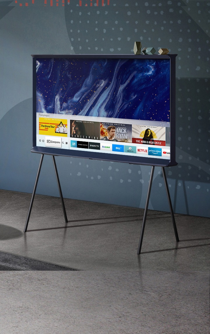 Dark Blue The Serif sits on a stand in front of a navy wall with graphic elements. With galactic swirls as the background on-screen, The Serif shows how it connects you with content you love, all in one place.